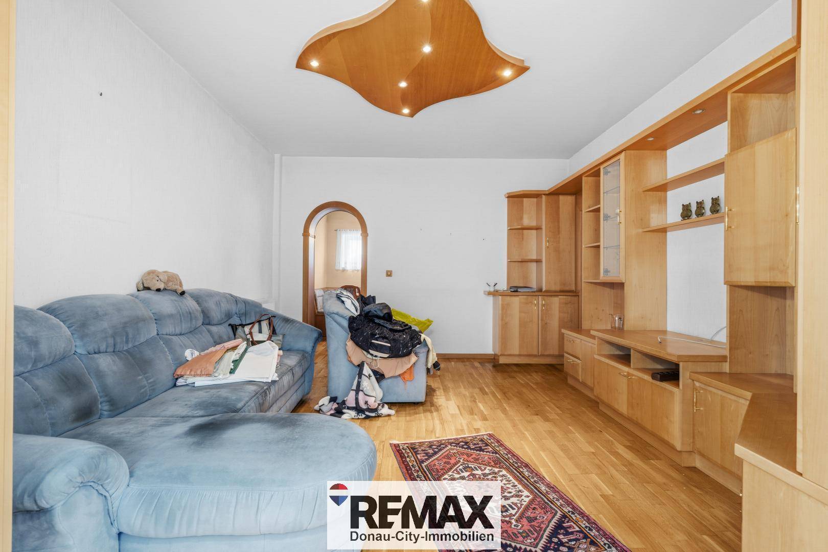 Wohnzimmer mit blauer Couch, Holzparkett und einer dekorativen Holzdecke.