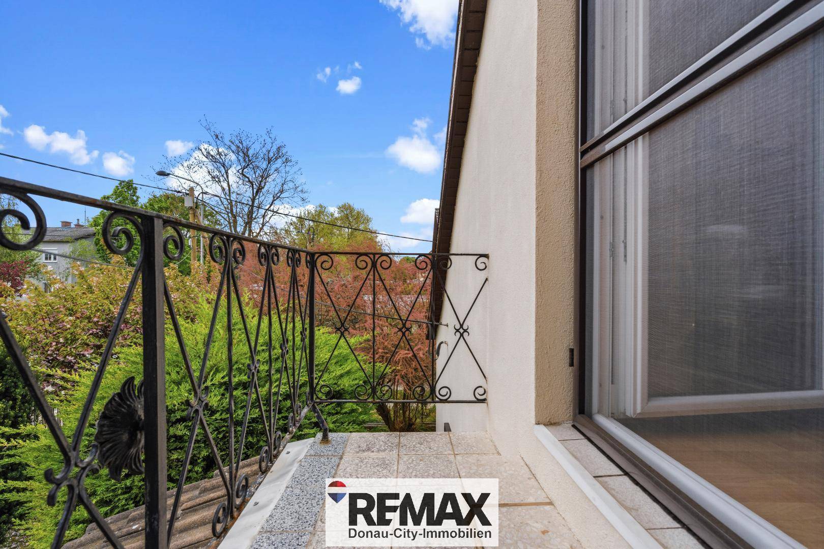 Kleiner Balkon mit schmiedeeisernem Geländer und Blick ins Grüne.