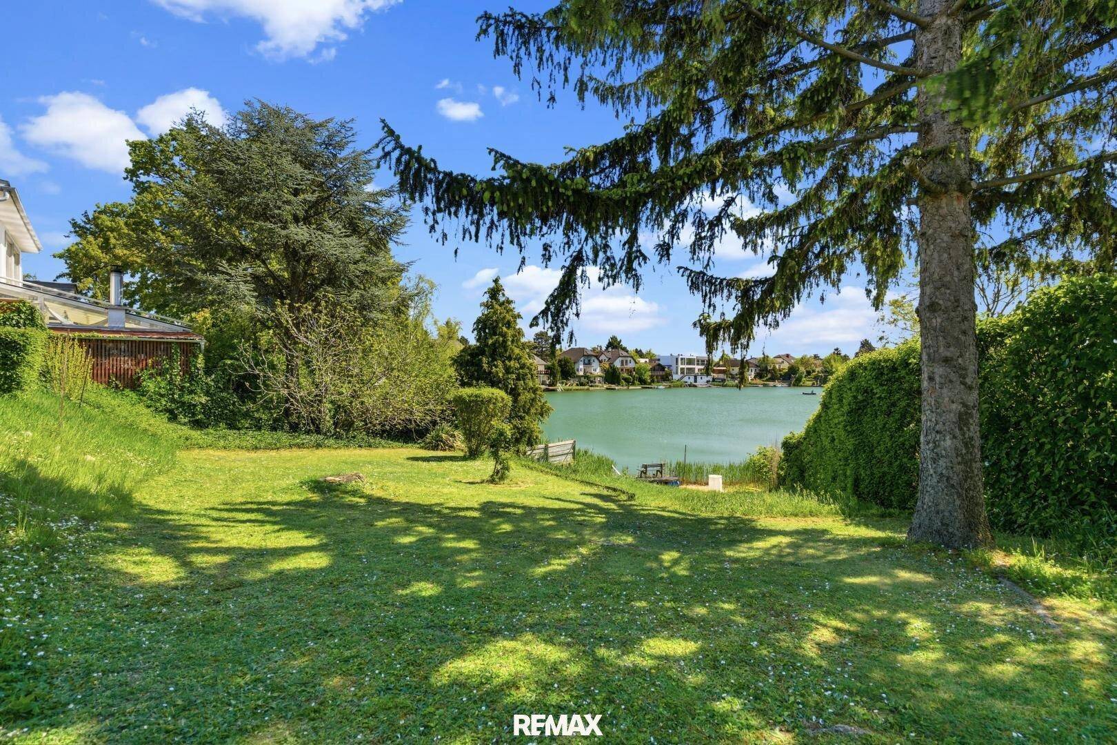 Große Rasenfläche im Garten mit Blick auf den See und umgebende Bäume.