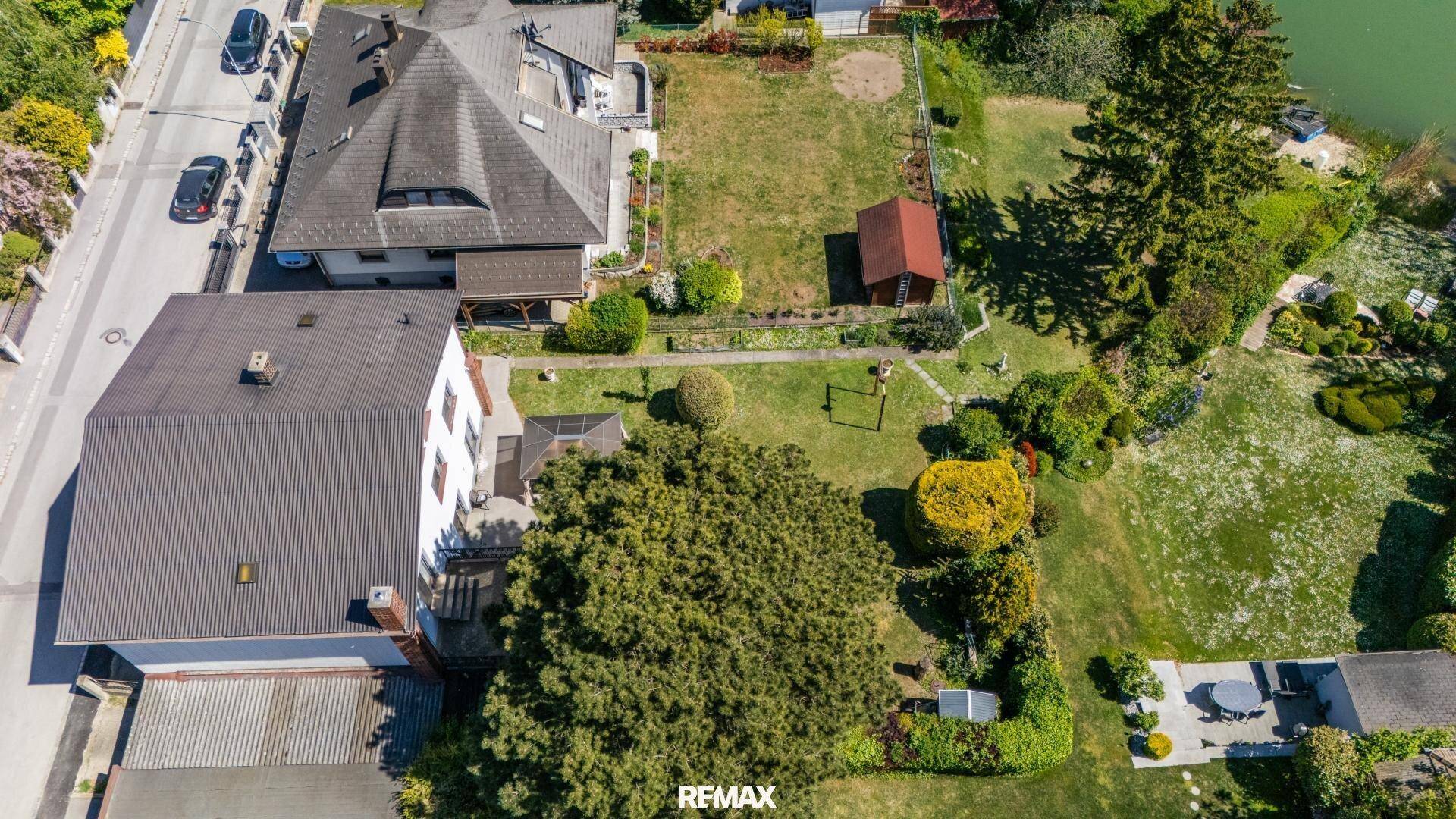 Luftaufnahme des Grundstücks mit Haus, Garten, Nebengebäude und angrenzendem See.
