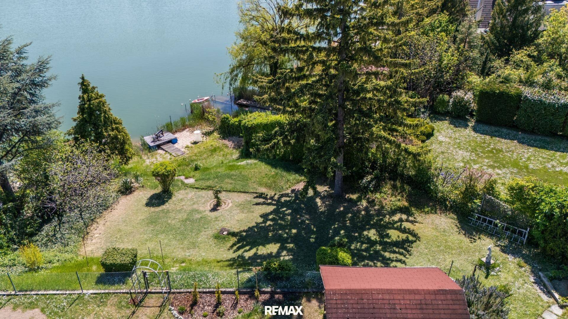 Gartenbereich mit direktem Zugang zum See, umgeben von Bäumen und üppigem Grün.