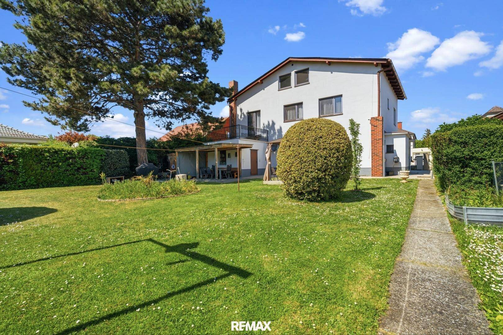 Großer, gepflegter Garten mit Rasenfläche, hohen Bäumen und dem Haus im Hintergrund.