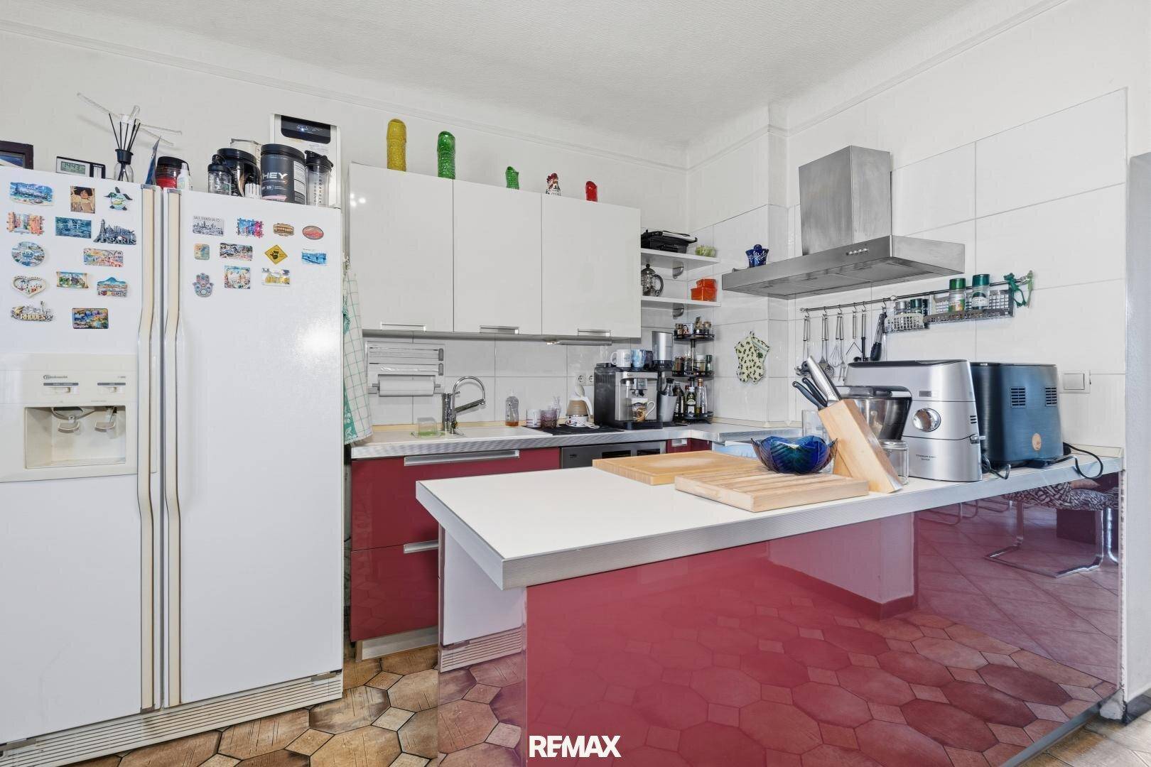 Moderne Küche mit roten und weißen Schränken, Kücheninsel und einem großen Kühlschrank.