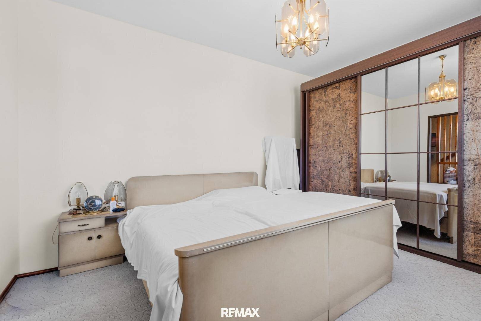 Helles Schlafzimmer mit Doppelbett, Spiegelschiebetüren und einem eleganten Kronleuchter an der Decke.