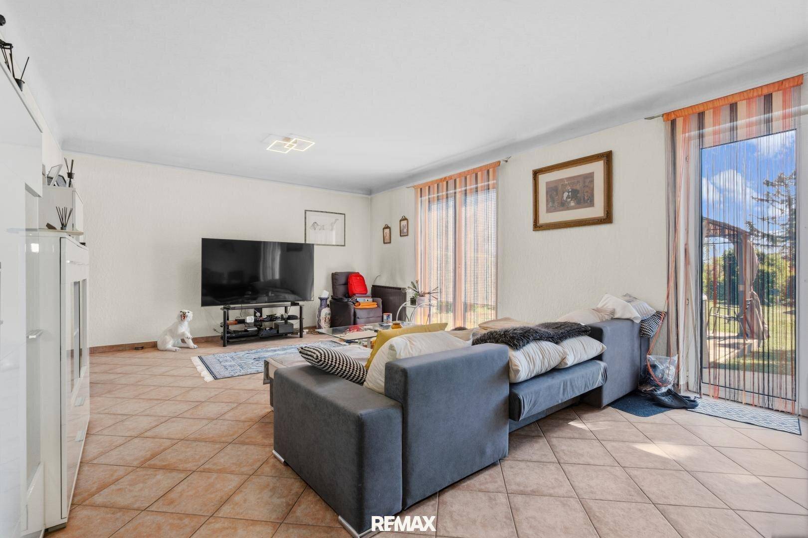 Helles Wohnzimmer mit Fliesenboden, großem Sofa und direktem Zugang zum Gartenbereich.