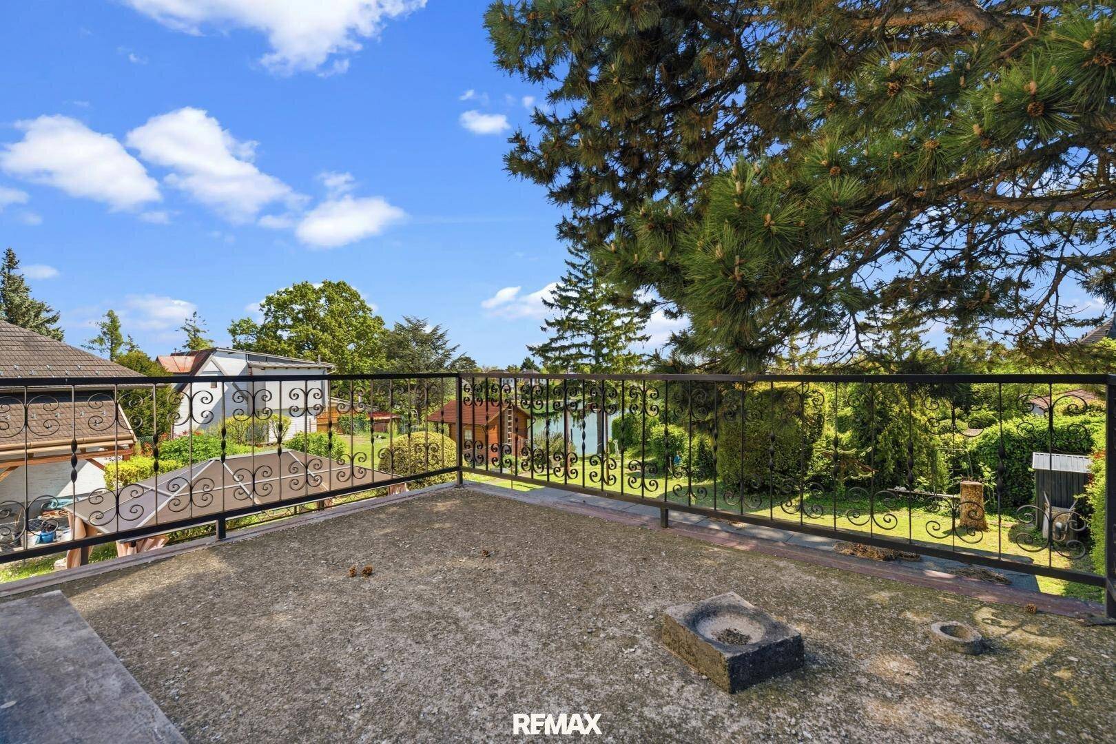 Offene Terrasse mit schmiedeeisernem Geländer und Blick auf den Garten und die umliegende Natur.