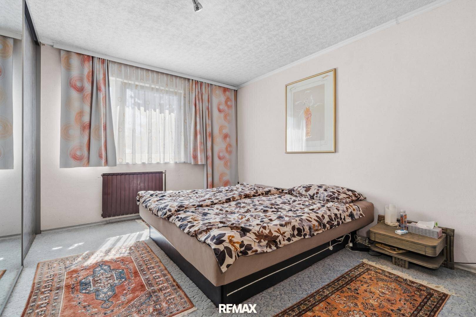 Schlafzimmer mit Doppelbett, Teppichboden und einem Fenster, das viel Tageslicht hereinlässt.