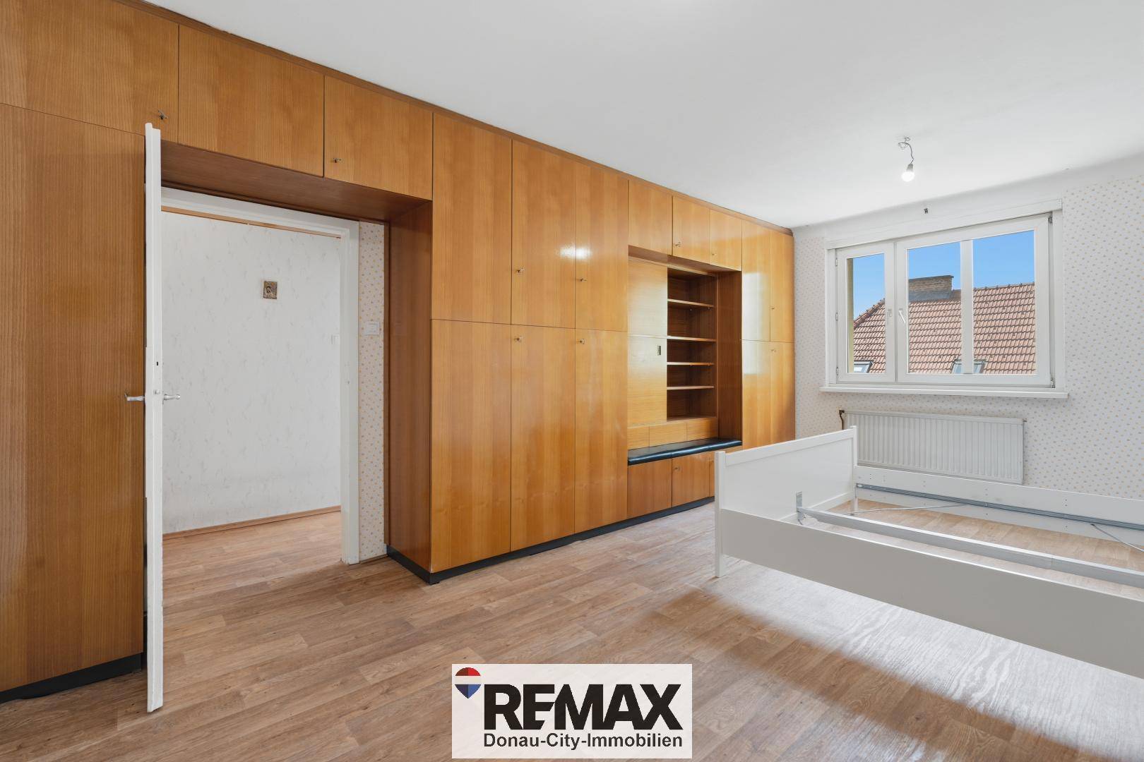 Schlafzimmer mit Einbauschränken aus Holz, Laminatboden und Fenster.