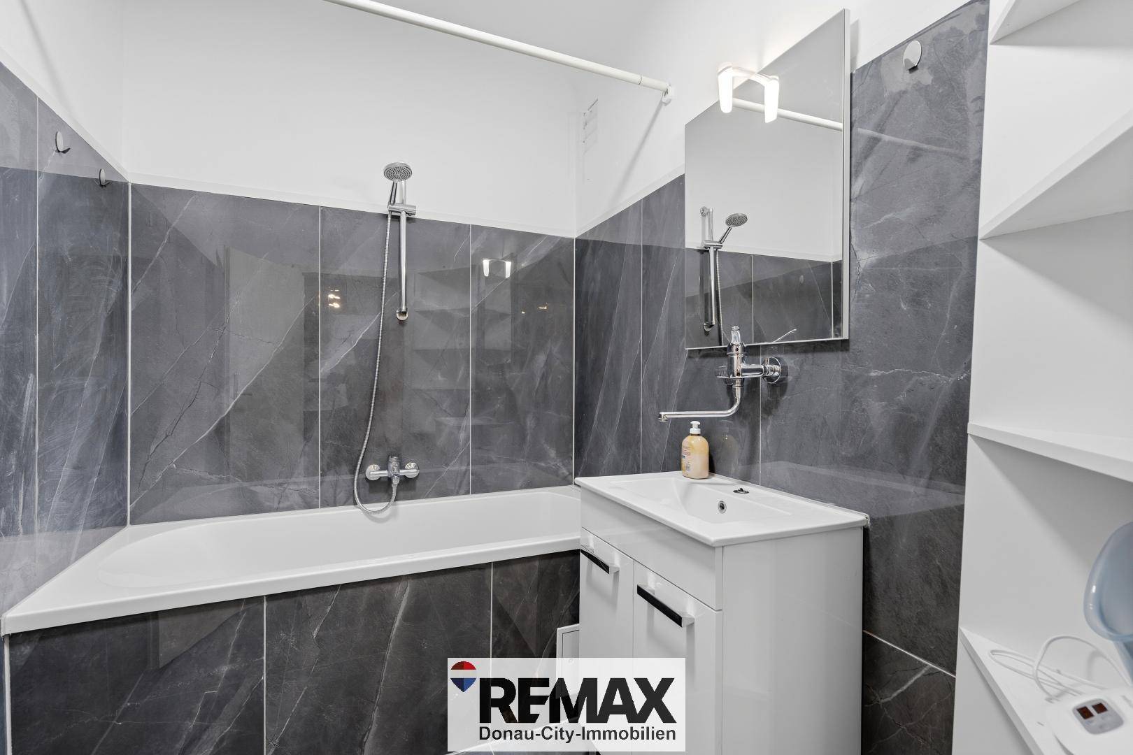 Modernes Badezimmer mit grauen Fliesen, Badewanne und Waschbecken.
