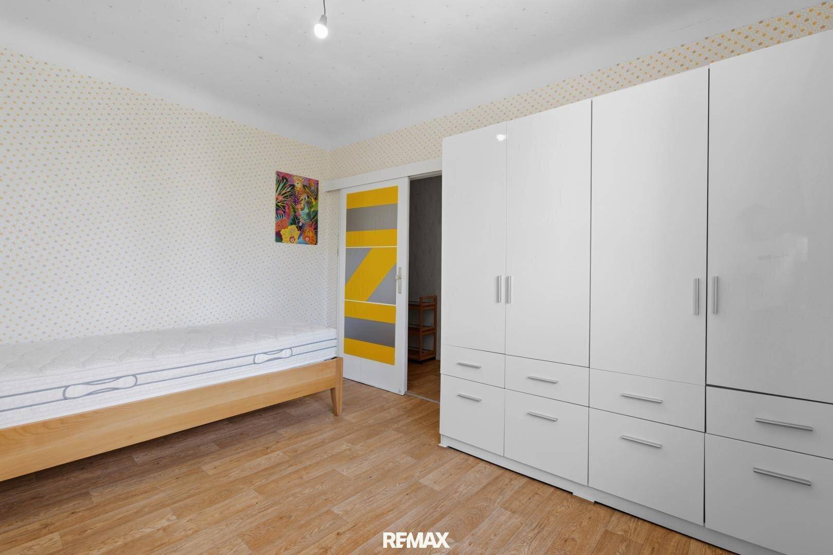 Schlafzimmer mit Holzboden, weißem Kleiderschrank und Schiebetür.