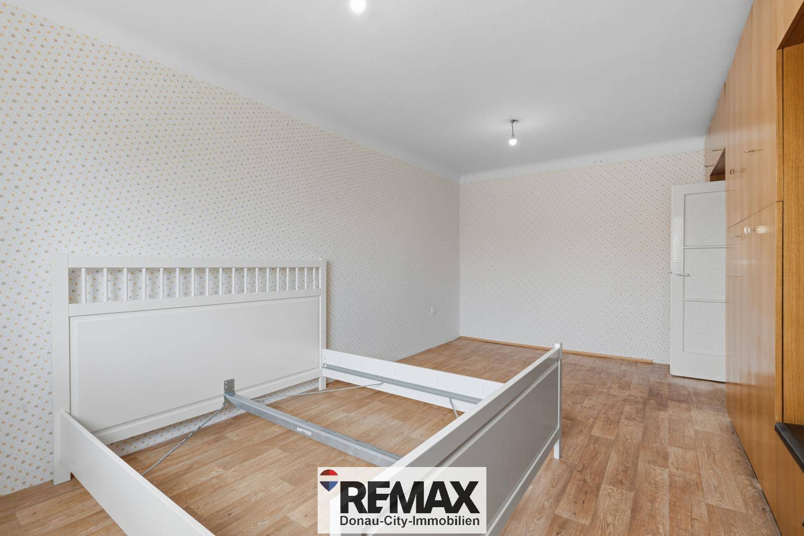 Schlafzimmer mit Laminatboden, gemusterter Tapete und einem weißen Bettrahmen.