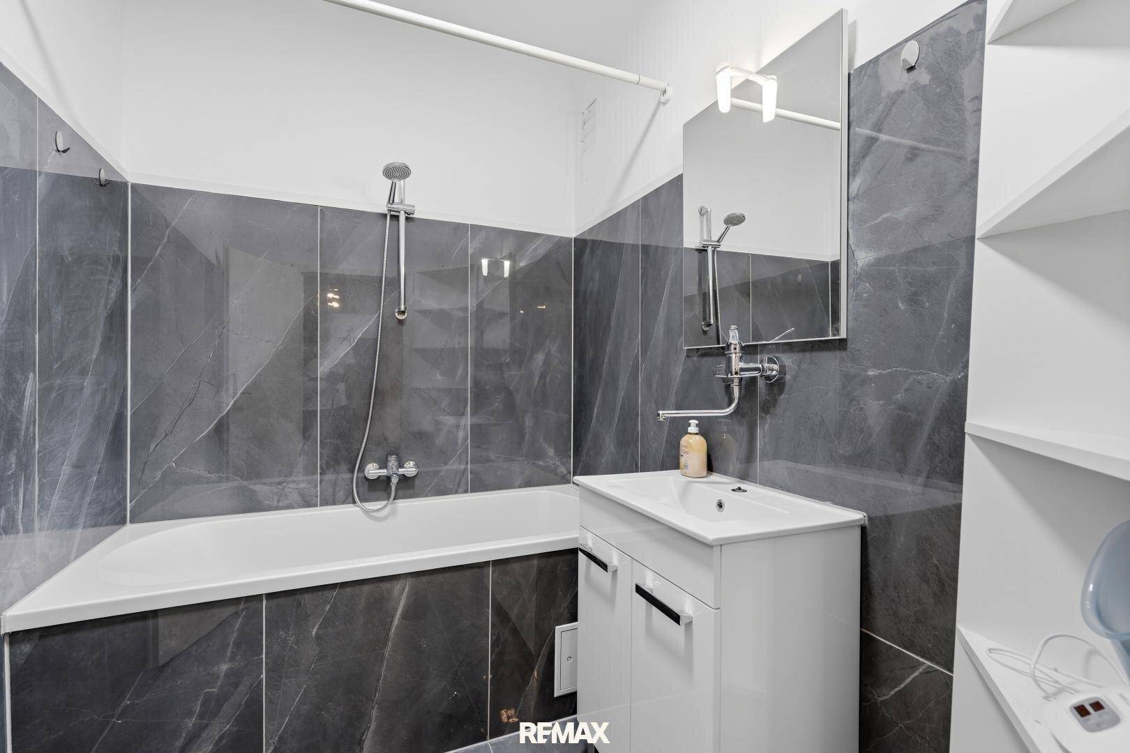 Modernes Badezimmer mit dunklen Marmorfliesen, Badewanne und Waschtisch.