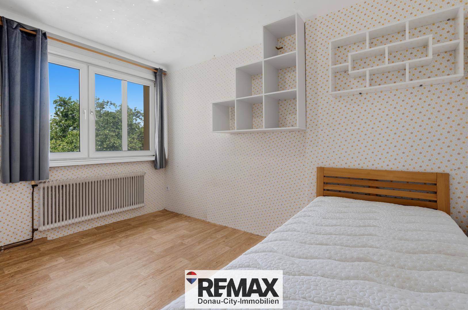 Schlafzimmer mit Einzelbett, Laminatboden und Fenster mit Blick ins Grüne.