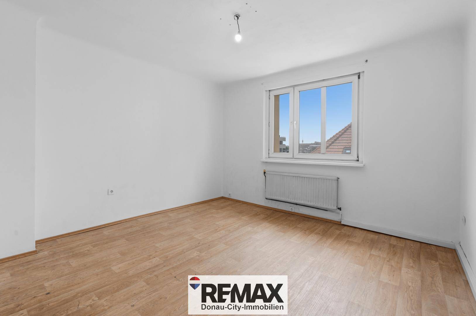 Leeres Wohnzimmer mit Laminatboden und Fenster, bereit zur individuellen Gestaltung.