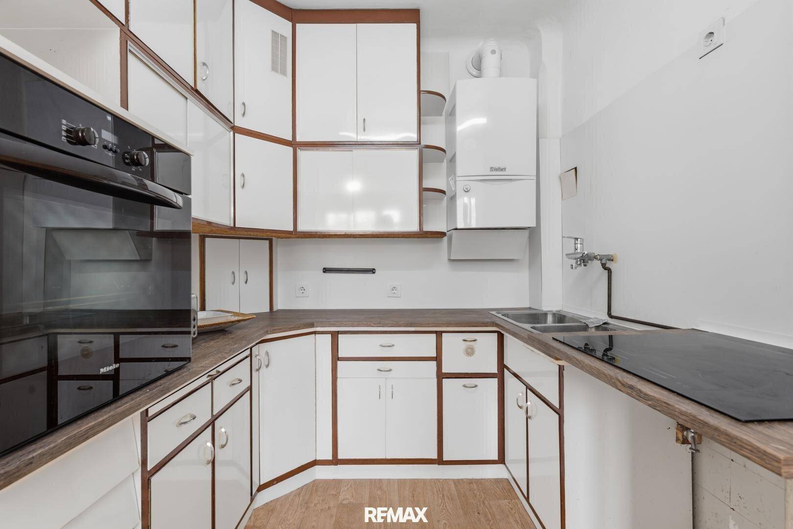 Funktionale Küche mit weißen Schränken, Holzdetails und integrierten Geräten.