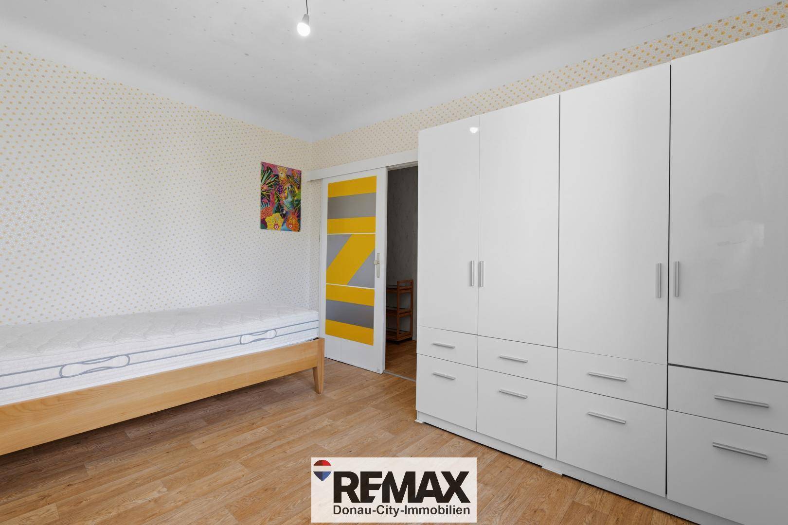 Schlafzimmer mit weißem Kleiderschrank, Einzelbett und farbiger Schiebetür.