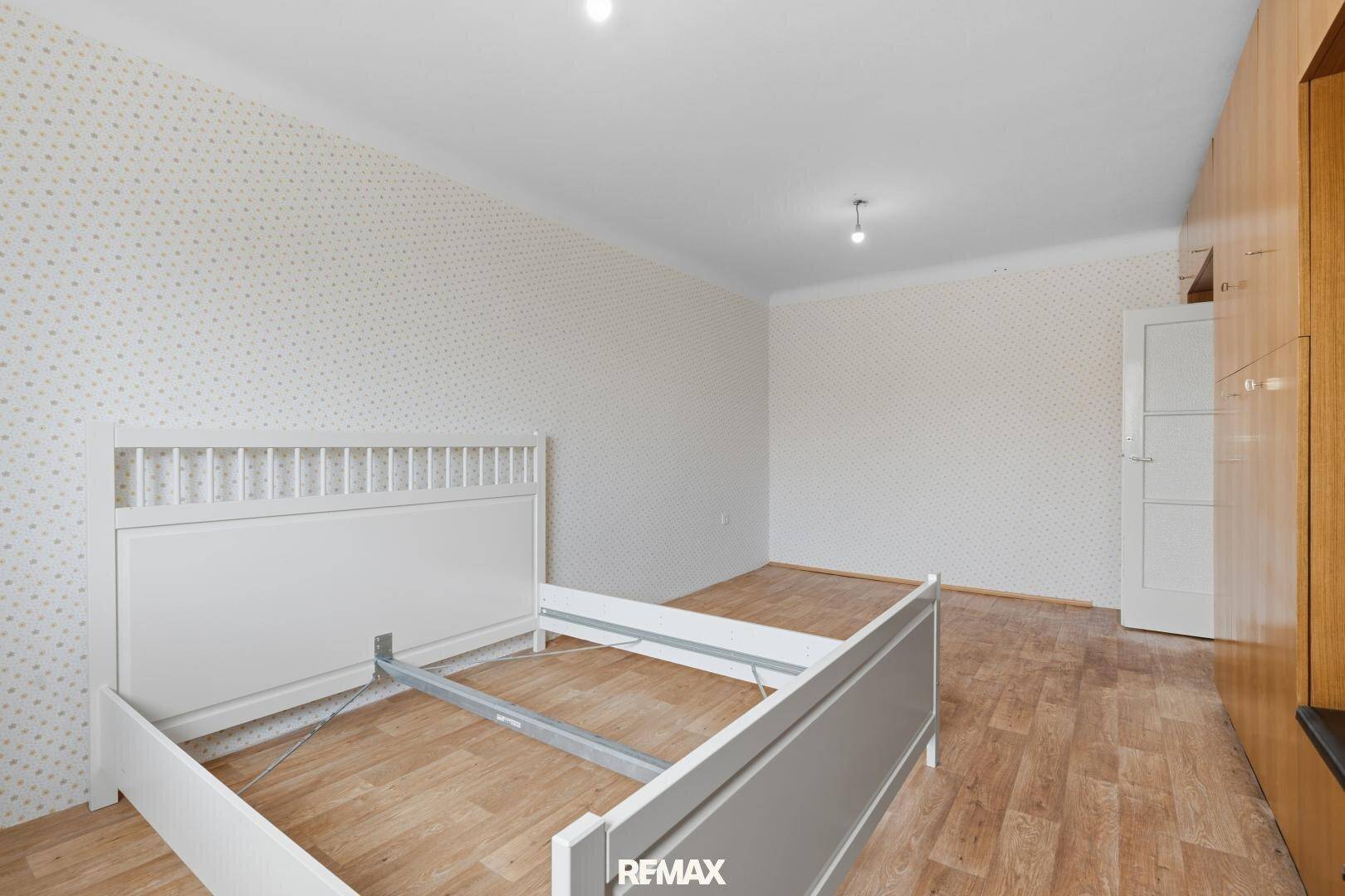 Schlafzimmer mit Holzboden, gemusterter Tapete und einem weißen Bettgestell.