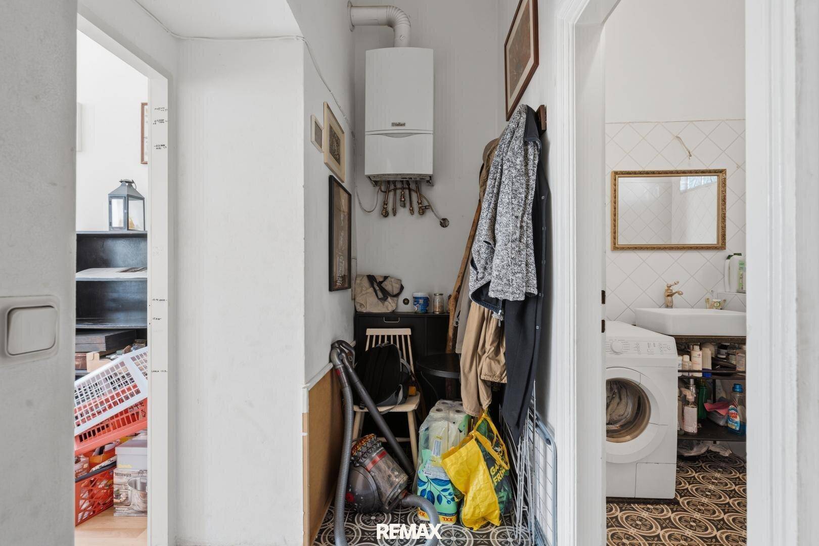 Flur mit Gastherme, Garderobe und Zugang zum Badezimmer, der als praktischer Hauswirtschaftsraum dient.