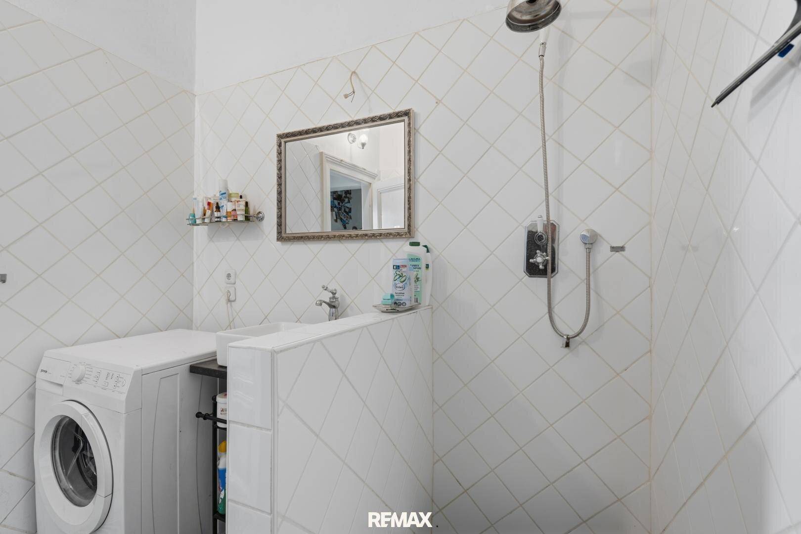 Badezimmer mit Duschbereich, Waschbecken und Waschmaschine, das funktional und hell gestaltet ist.