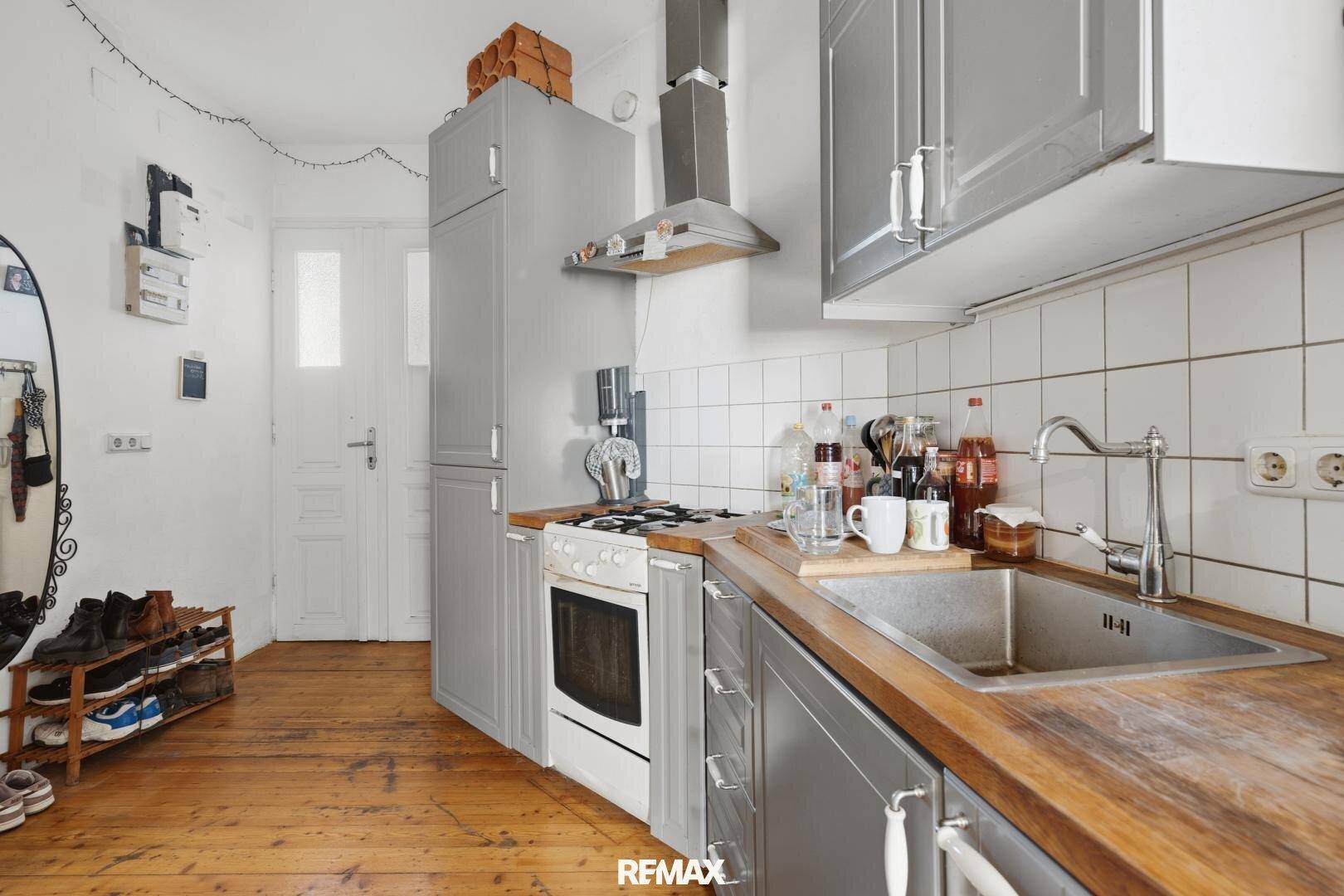 Funktionale Küche mit grauen Fronten, Spüle und Holz-Arbeitsplatte auf Dielenboden, die zum Kochen einlädt.