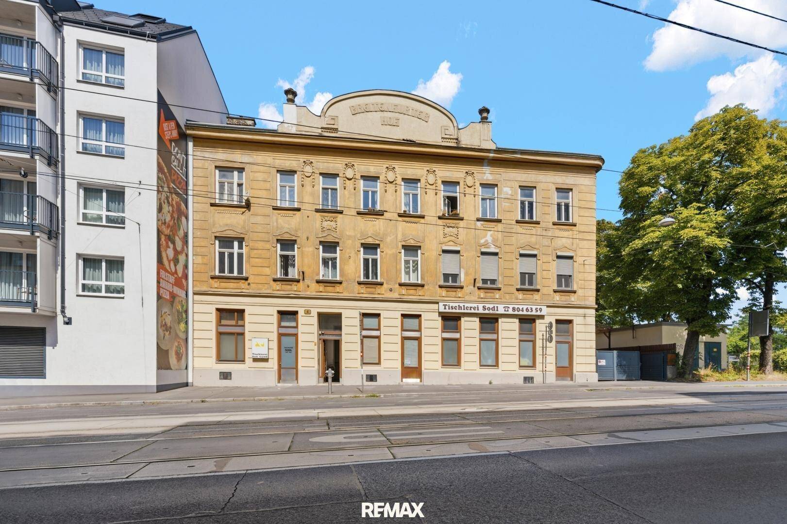 Historisches Gebäude mit klassischer Fassade und Geschäften im Erdgeschoss, das sich in einer städtischen Umgebung befindet.