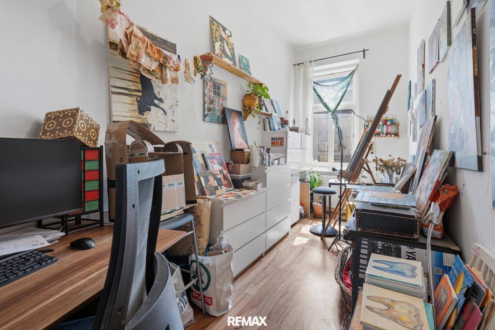 Kreatives Arbeitszimmer mit vielen Kunstwerken, Schreibtisch und Fenster, das zum Arbeiten und Inspirieren einlädt.