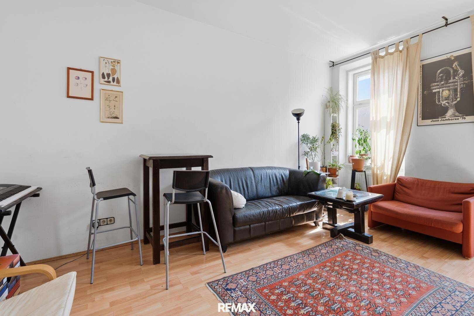 Helles Wohnzimmer mit Ledersofa, Stehtisch und Teppich auf Holzboden, das eine einladende Atmosphäre schafft.