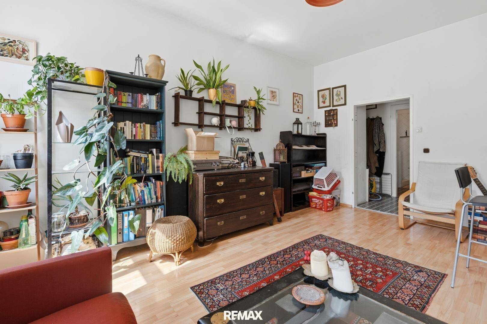 Gemütliches Wohnzimmer mit Bücherregal, Kommode und Teppich auf Holzboden, ideal zum Entspannen und Lesen.