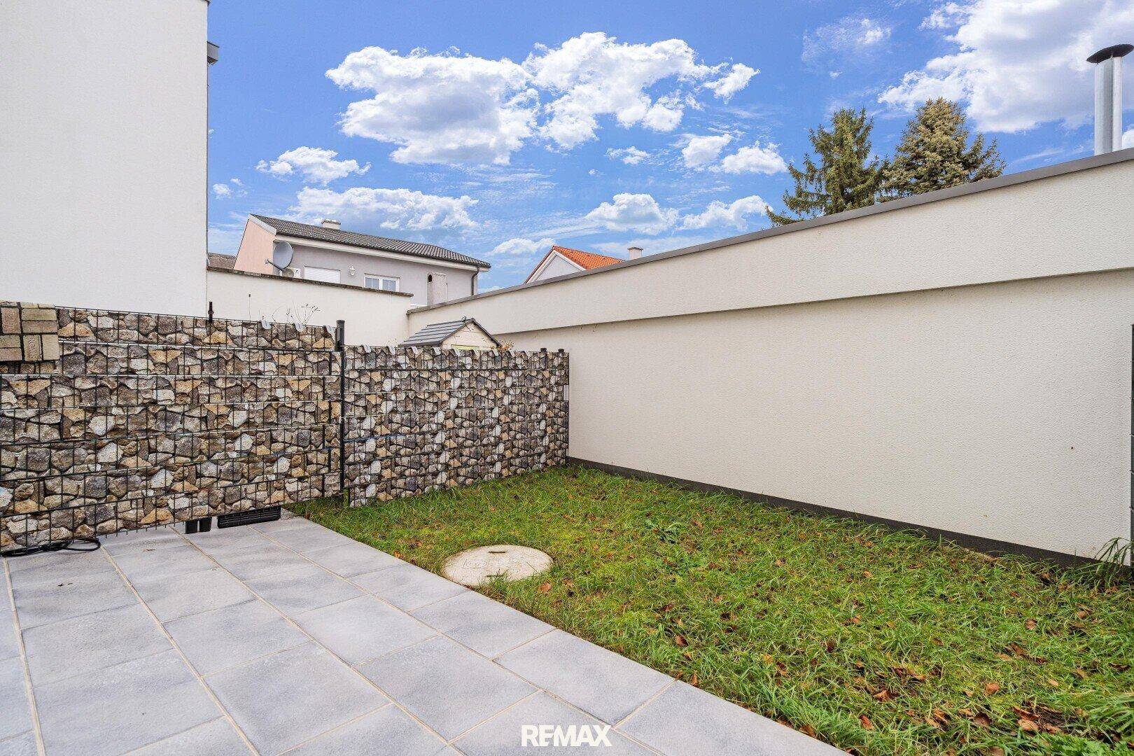 Kleiner Gartenbereich mit Rasenfläche und gepflasterter Terrasse, umgeben von Gabionen.