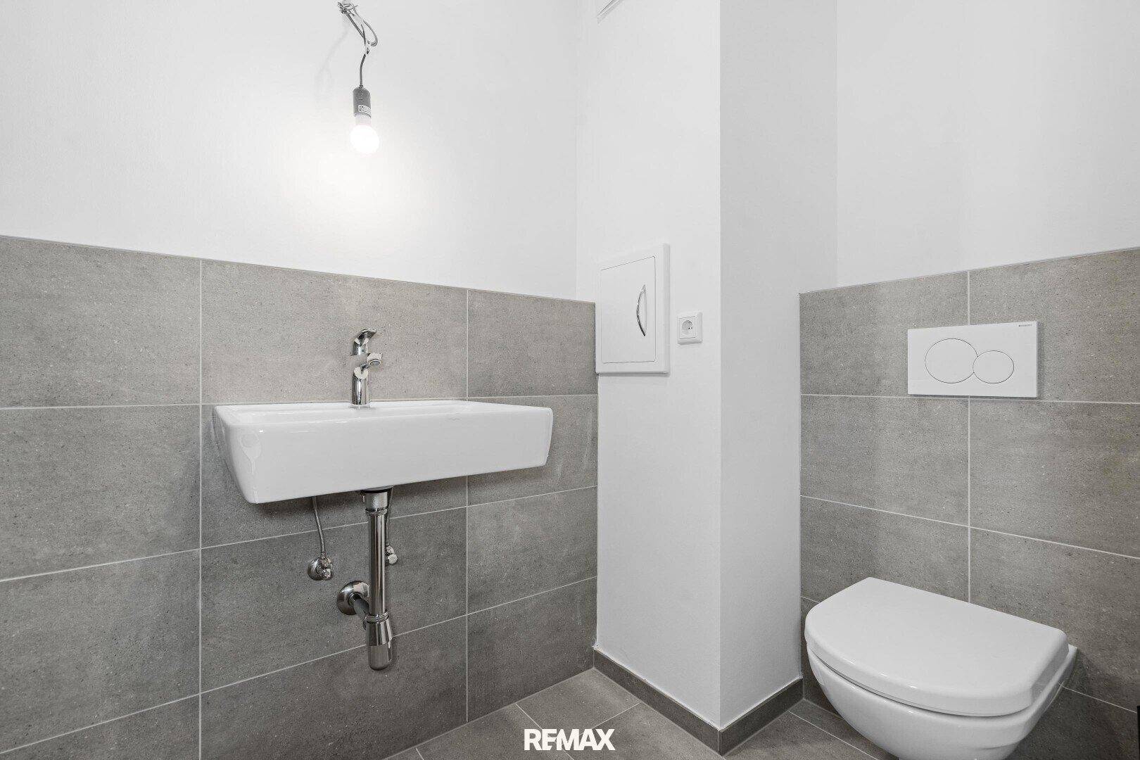 Modernes Gäste-WC mit Wand-WC und Waschbecken, graue Fliesen und weiße Wände.
