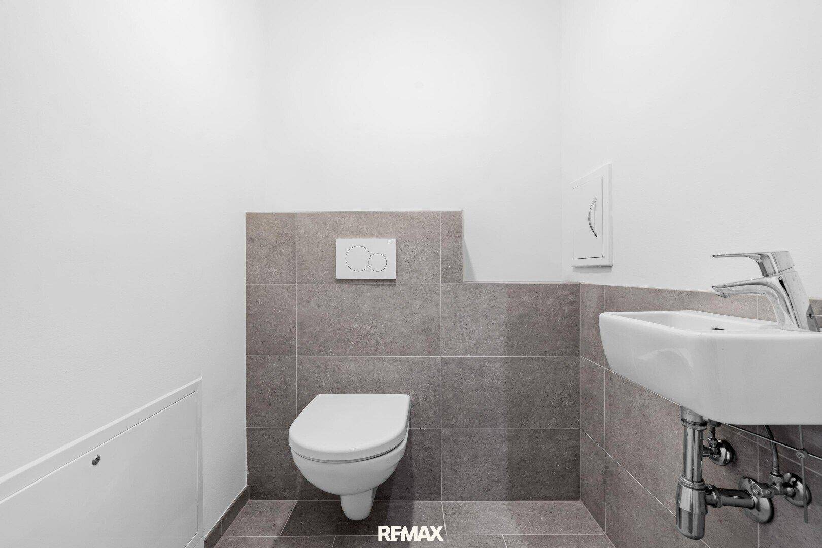 Modernes Gäste-WC mit Wand-WC und kleinem Waschbecken, graue Fliesen.