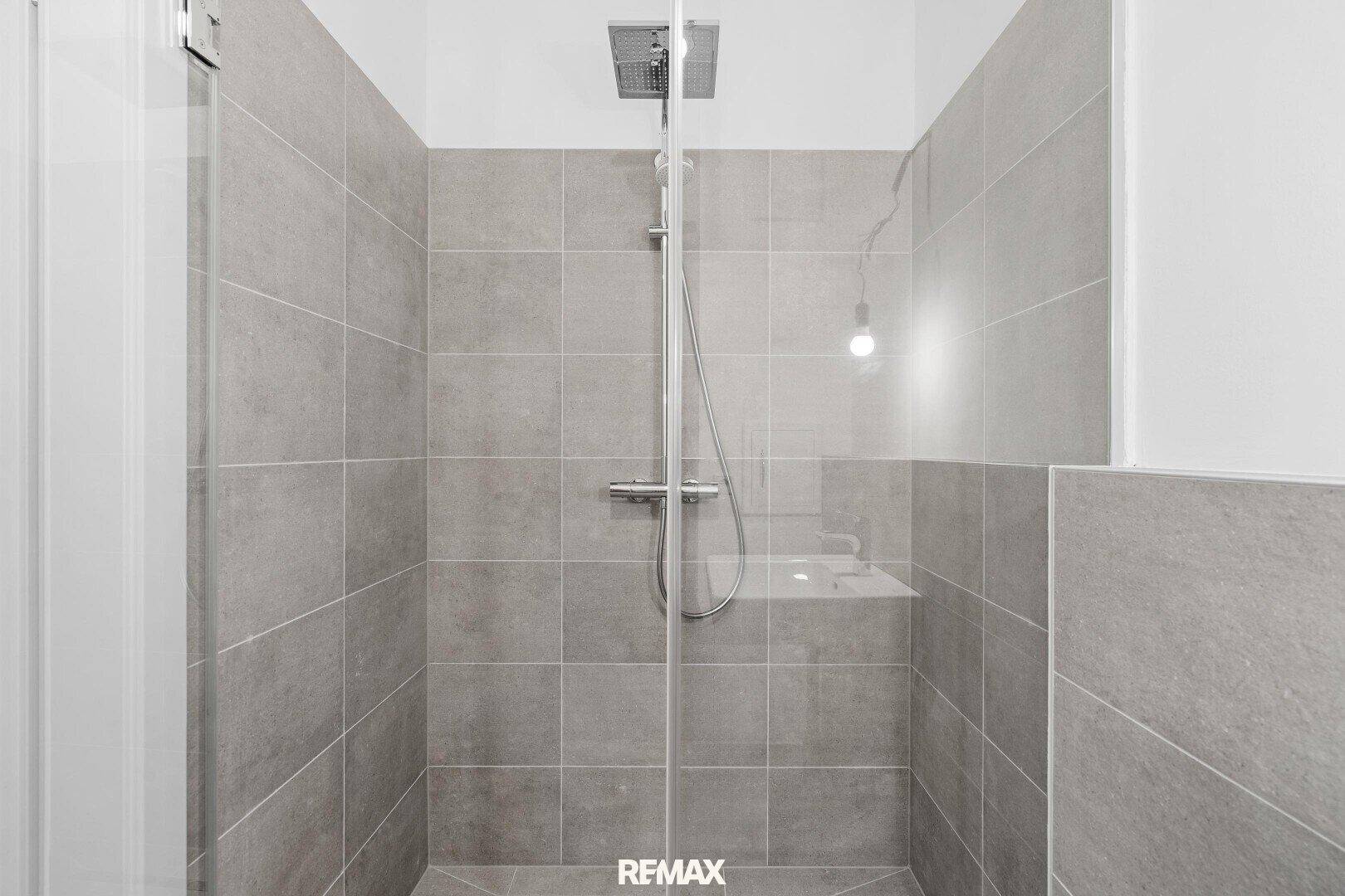 Ebenerdige Dusche mit Glasabtrennung in einem modern gefliesten Badezimmer.