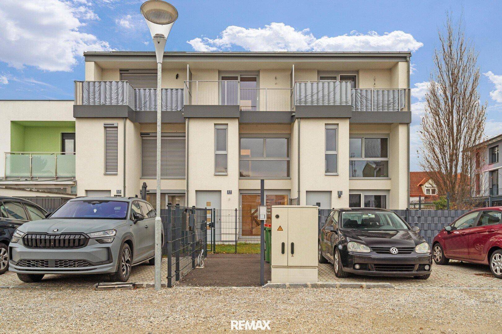 Vorderansicht moderner Reihenhäuser mit Parkplätzen und gepflegter Fassade, einladend und funktional.