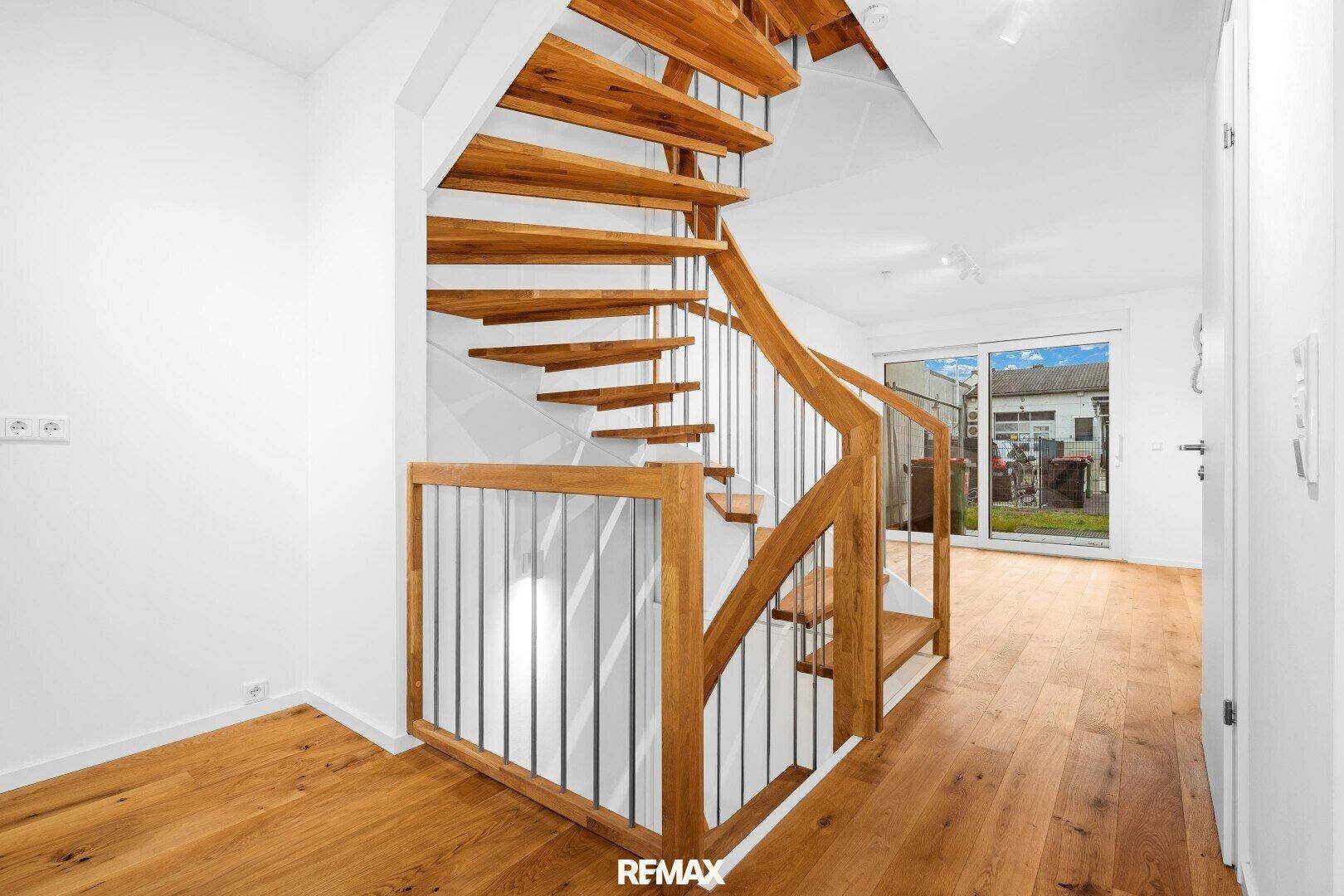 Elegante Holztreppe mit Metallgeländer in einem hellen Flur mit Holzboden.