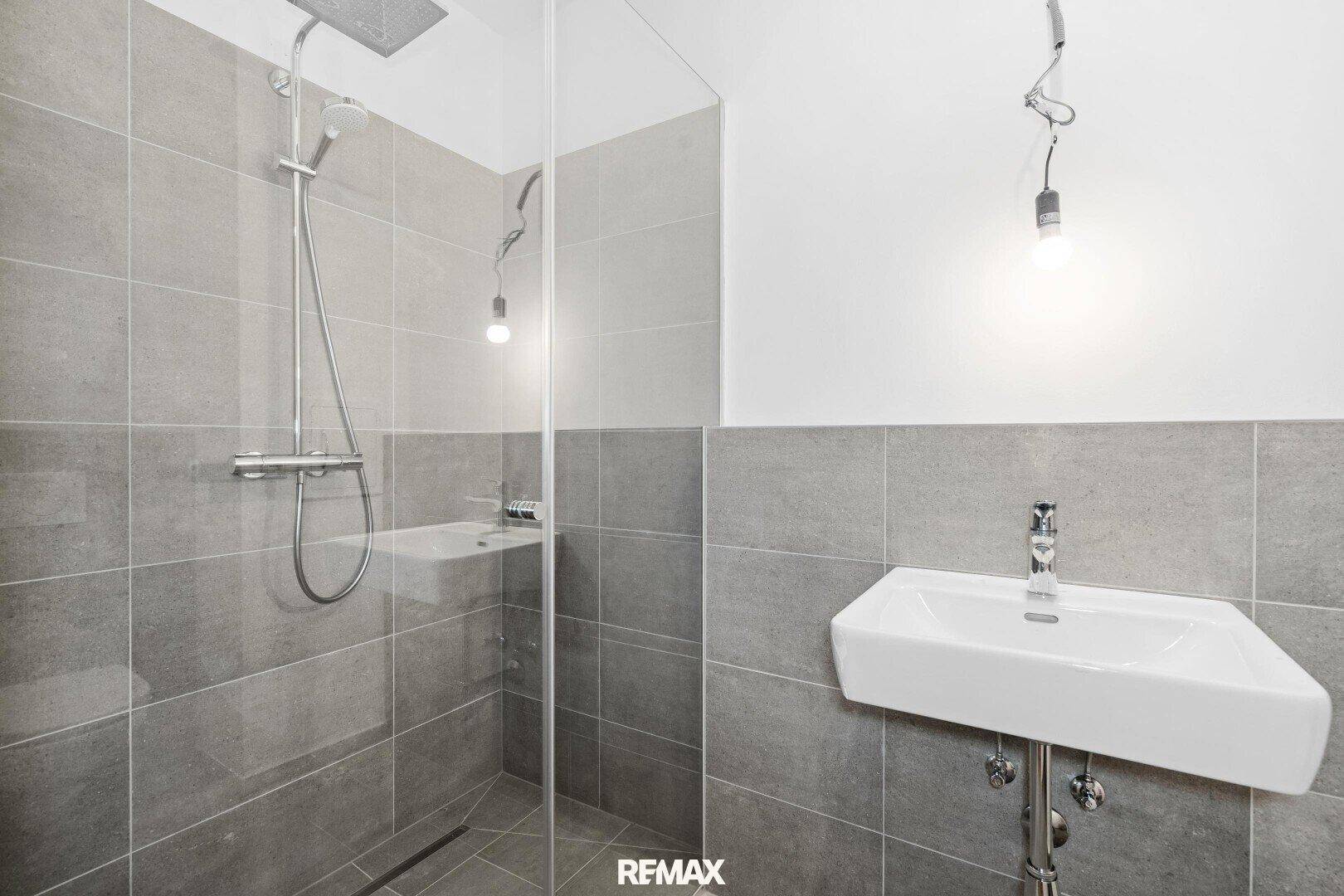 Modernes Badezimmer mit ebenerdiger Dusche und Waschbecken, graue Fliesen.