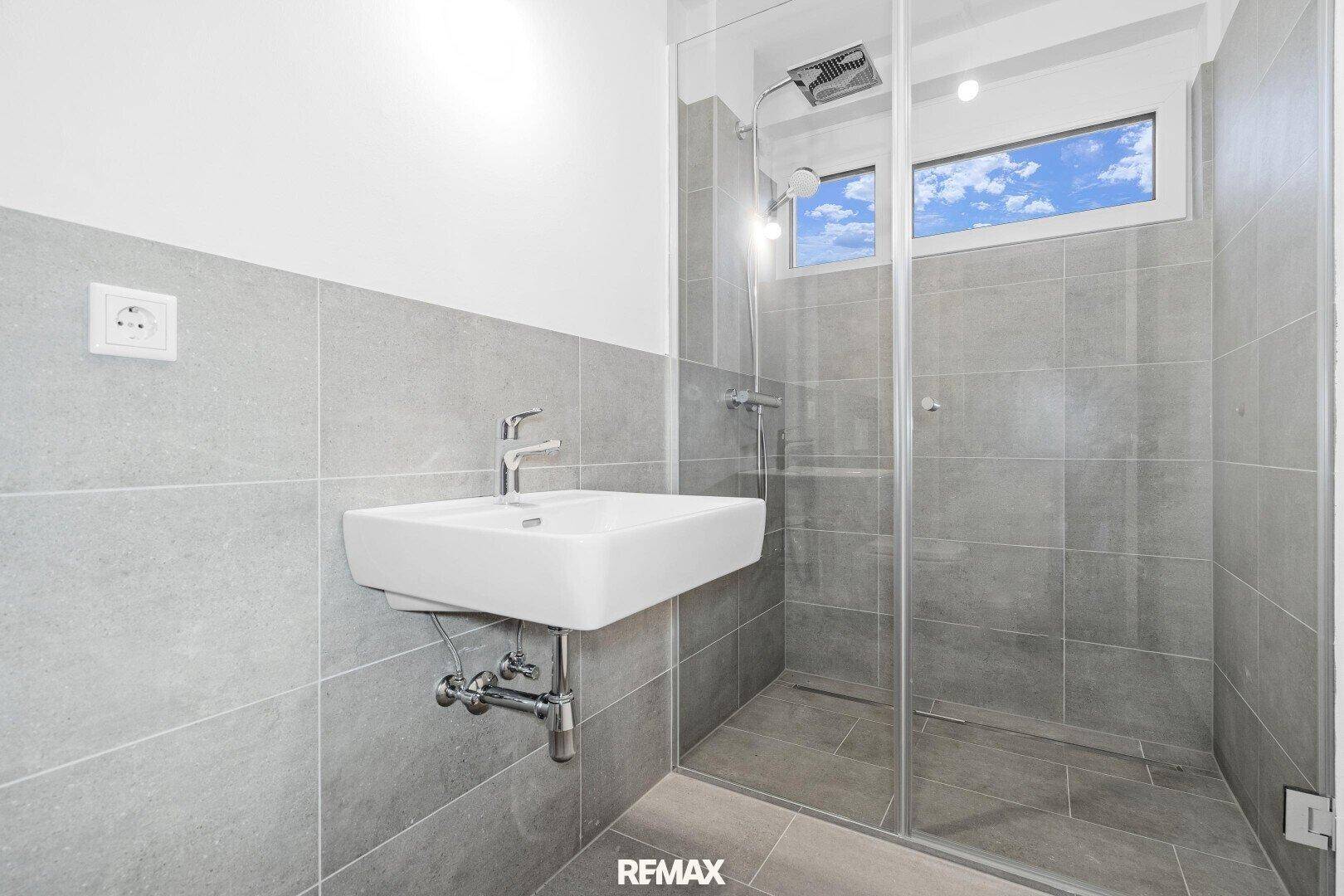 Modernes Badezimmer mit ebenerdiger Dusche, Waschbecken und Fenster.