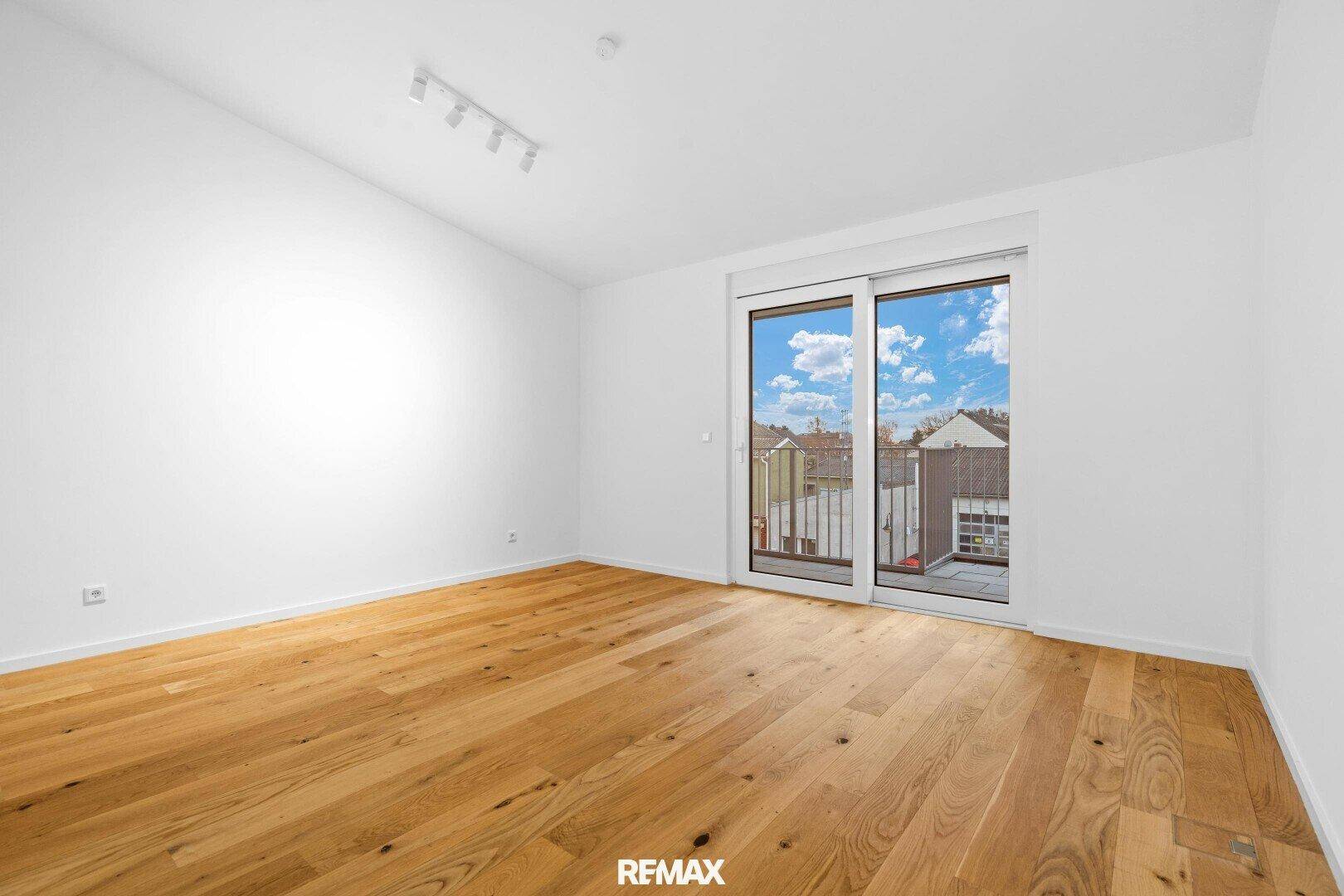 Leerer Raum mit Holzboden und Schiebetür zum Balkon, hell und geräumig.