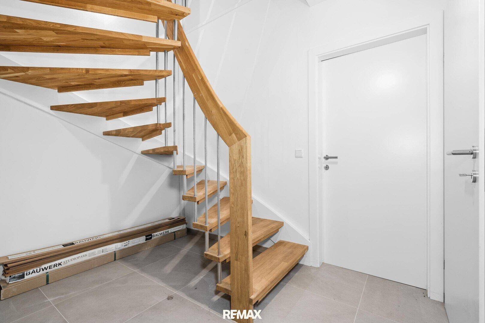 Heller Flur mit moderner Holztreppe und Fliesenboden, der die verschiedenen Etagen stilvoll verbindet.