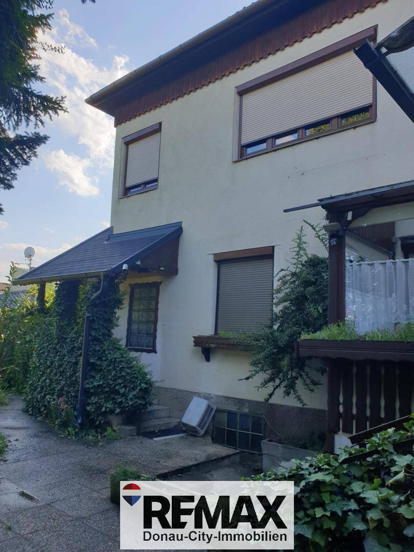 Seitenansicht des Hauses mit Rollläden an den Fenstern und üppiger Begrünung.
