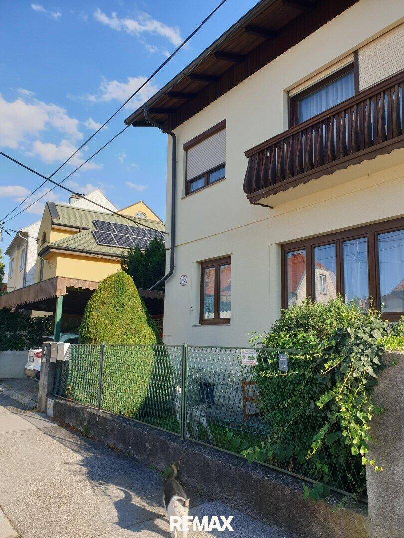Ansicht des Hauses von der Straße mit Balkon, grüner Hecke und Photovoltaikanlage auf dem Nachbardach.