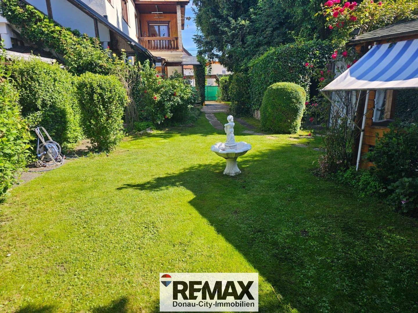Gepflegter Garten mit Rasenfläche, einem Brunnen und einem kleinen Zelt im Hintergrund.