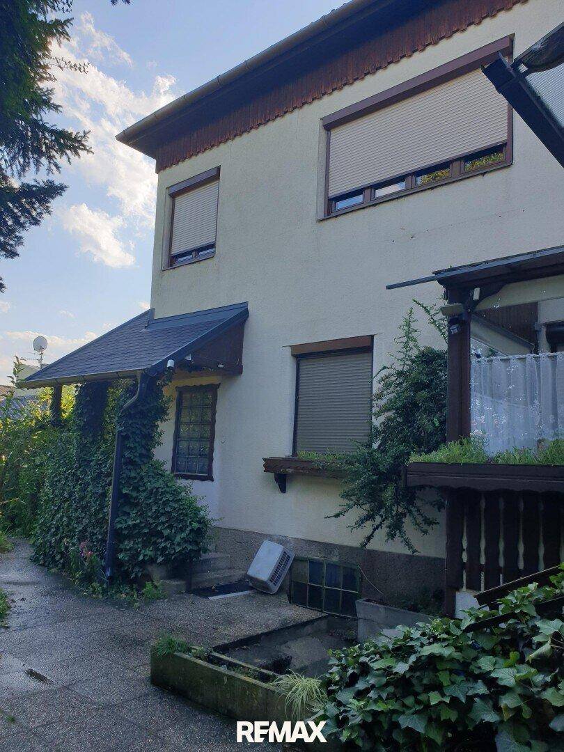 Seitenansicht des Hauses mit Rollläden an den Fenstern und einer begrünten Fassade.