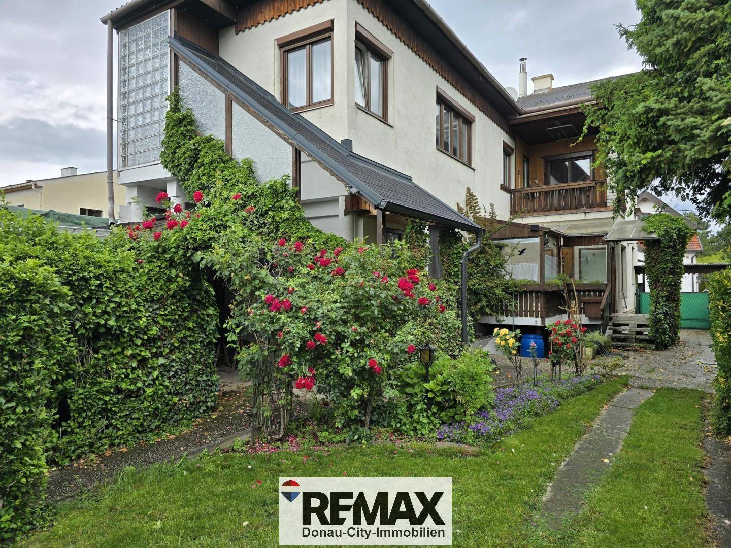 Rückseite des Hauses mit Garten, blühenden Rosen und einem Weg durch das Grün.