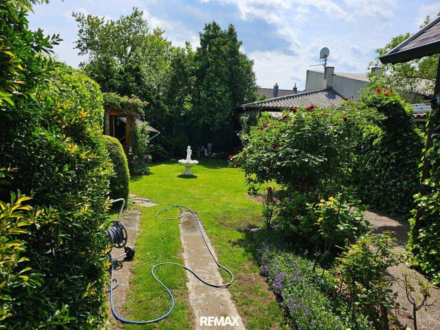 Gepflegter Gartenbereich mit Rasenfläche, Gartenweg und einem dekorativen Brunnen neben dem Haus.