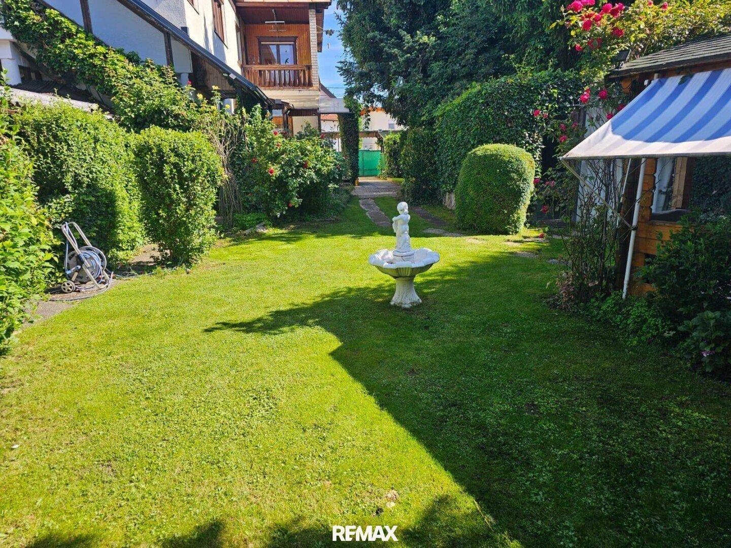 Weitläufiger Garten mit Rasenfläche, dekorativem Brunnen und einem kleinen Pavillon.