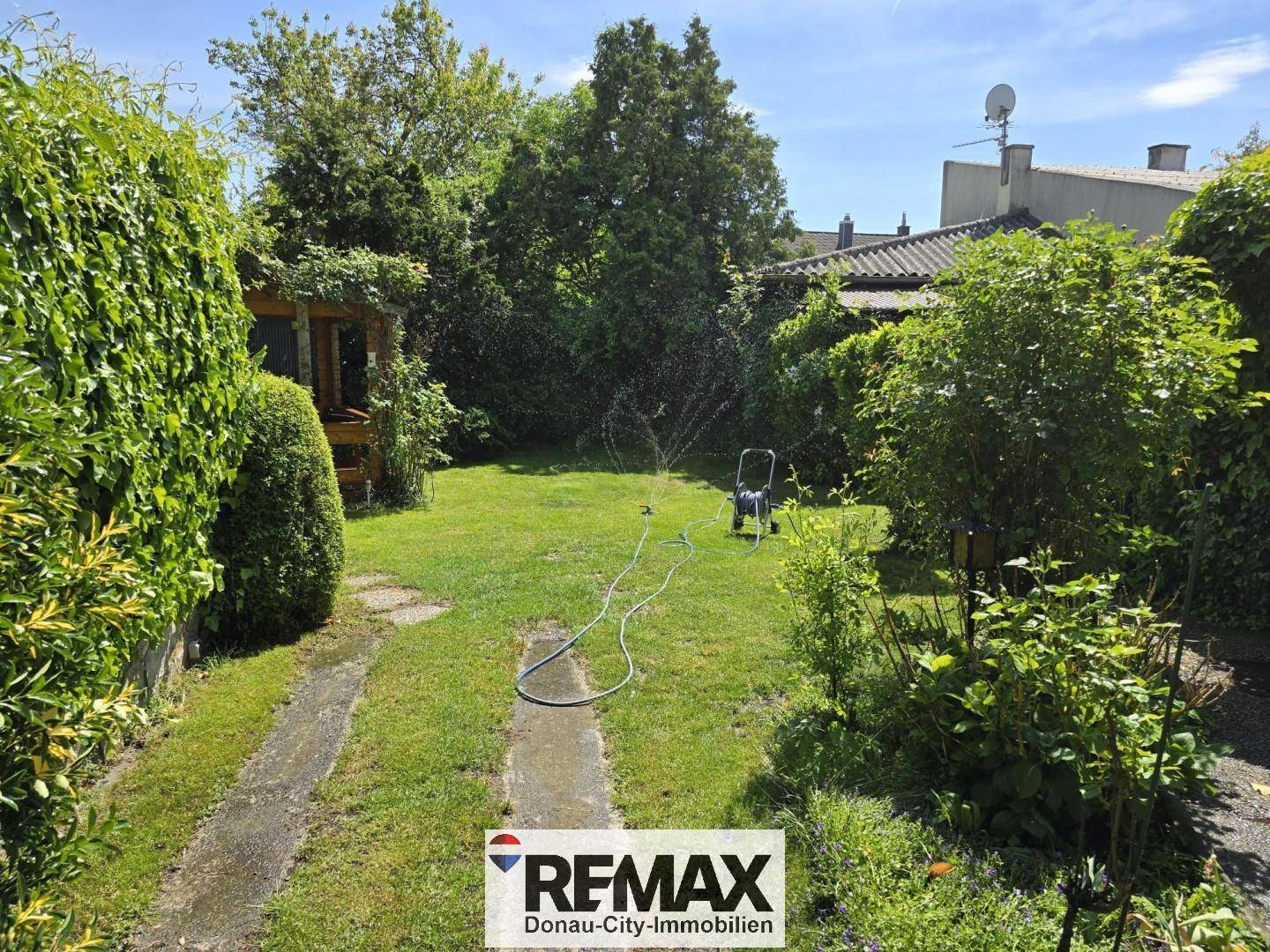 Großer, gepflegter Garten mit Rasenfläche und Bewässerungssystem an einem sonnigen Tag.