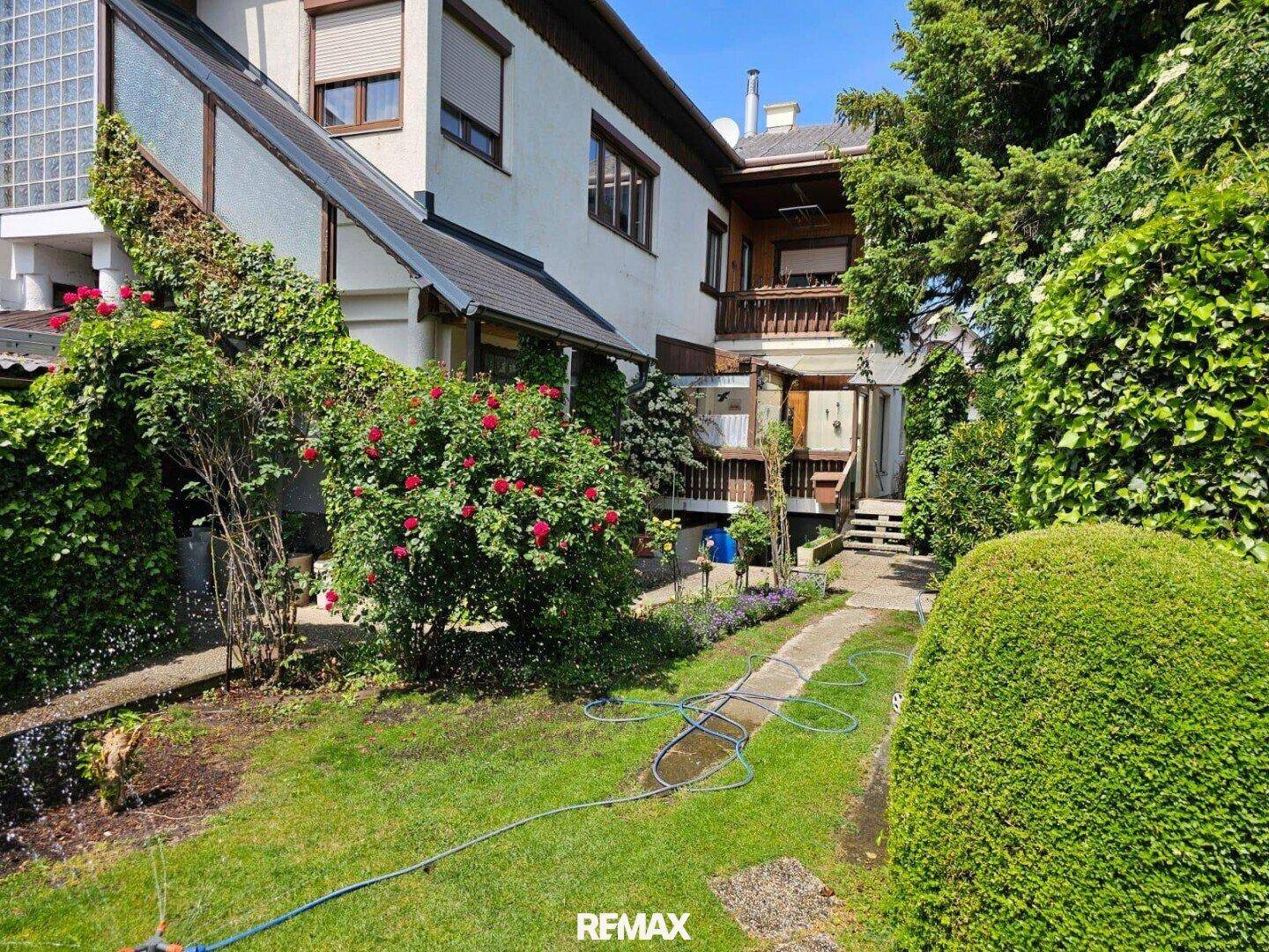 Gepflegter Gartenweg entlang des Hauses mit blühenden Rosen und grünen Büschen.
