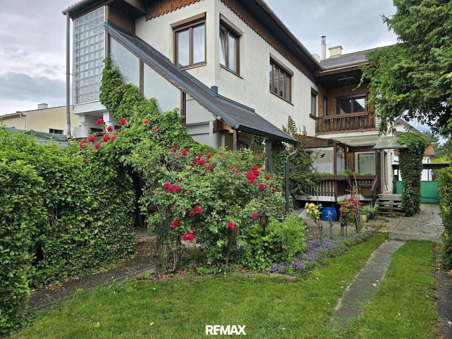 Rückansicht des Hauses mit Garten, Rosenbüschen und einem verglasten Anbau.