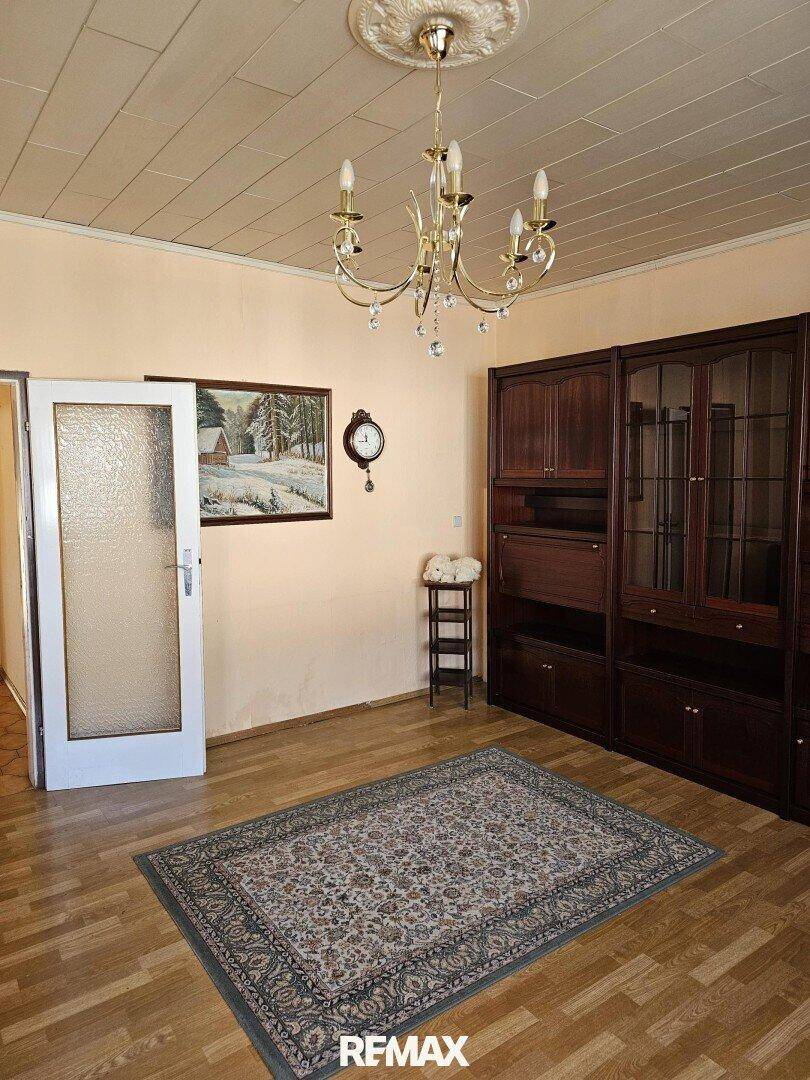 Heller Raum mit Parkettboden, großem Holzschrank und einem dekorativen Teppich, ideal als Wohnzimmer.