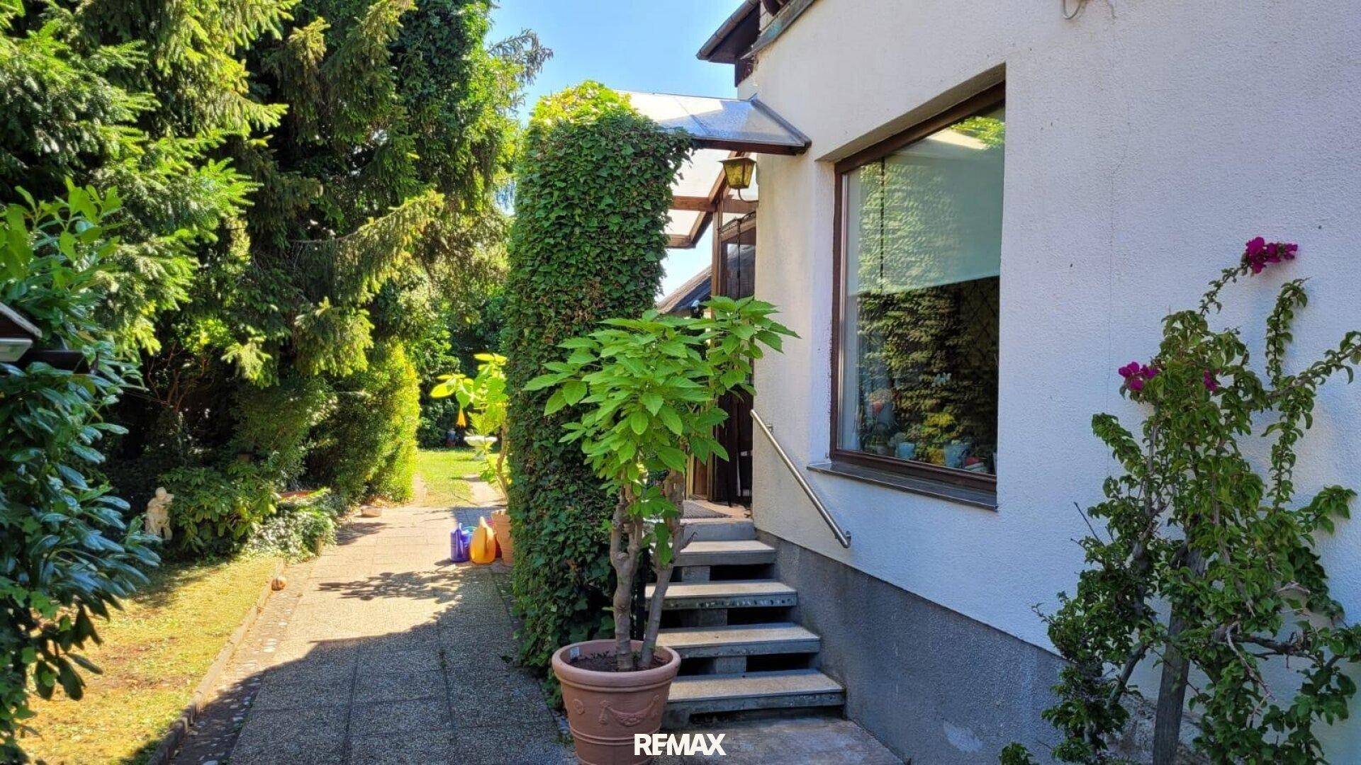 Eingangsbereich des Hauses mit Treppe, umgeben von üppiger grüner Bepflanzung.